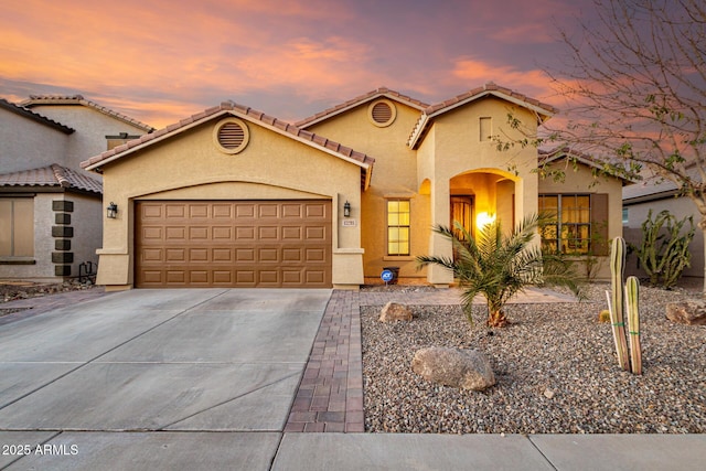 mediterranean / spanish-style home featuring concrete driveway, an attached garage, a tiled roof, and stucco siding