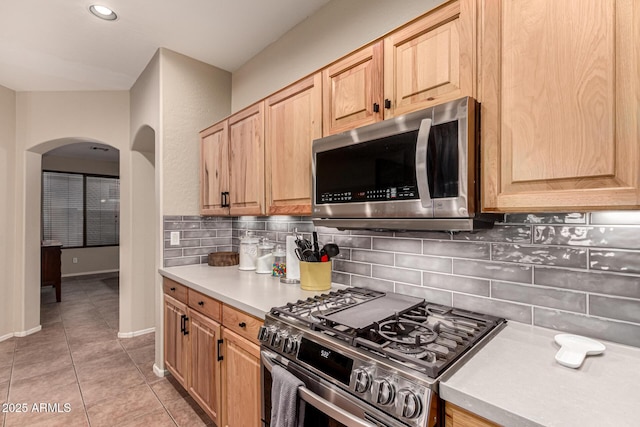 kitchen with arched walkways, tasteful backsplash, light countertops, appliances with stainless steel finishes, and light tile patterned flooring