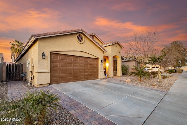 mediterranean / spanish-style home featuring a garage, driveway, a tile roof, a gate, and stucco siding