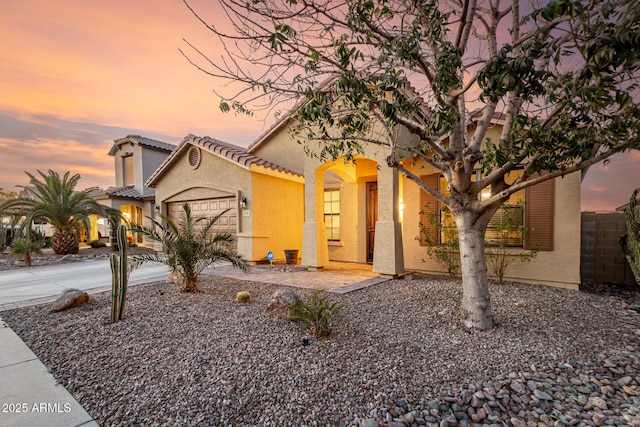 mediterranean / spanish-style home featuring a tile roof, stucco siding, fence, a garage, and driveway