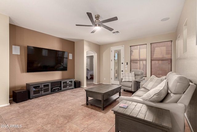 living area featuring arched walkways, light tile patterned floors, visible vents, a ceiling fan, and baseboards