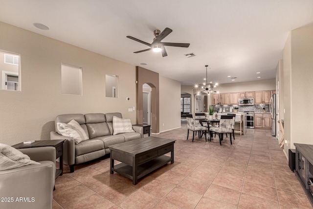 living area featuring light tile patterned floors, visible vents, arched walkways, and ceiling fan with notable chandelier