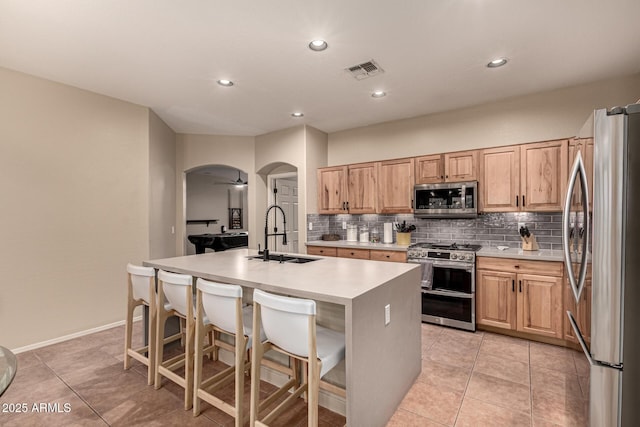 kitchen featuring arched walkways, stainless steel appliances, visible vents, a kitchen island with sink, and a sink