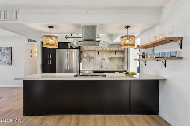 kitchen featuring kitchen peninsula, island range hood, hanging light fixtures, and stainless steel refrigerator