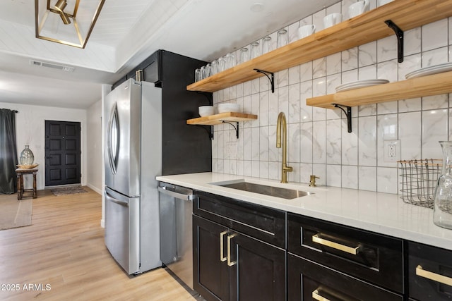 kitchen with sink, light wood-type flooring, tasteful backsplash, and appliances with stainless steel finishes