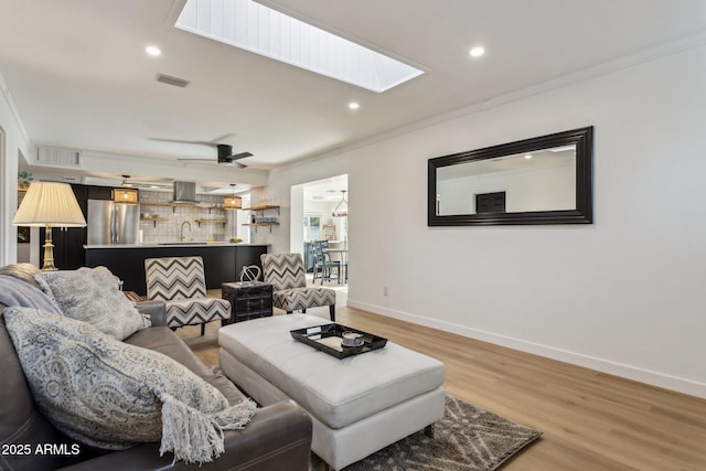 living room with crown molding, ceiling fan, sink, light wood-type flooring, and a skylight