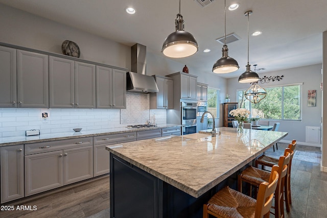 10207 W Hedge Hog Pl, Peoria, AZ 85383 - kitchen with wall chimney range hood, appliances with stainless steel finishes, recessed lighting, gray cabinetry, and a breakfast bar area