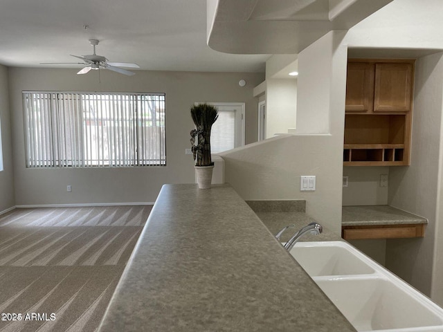 kitchen with baseboards, a ceiling fan, carpet, and a sink