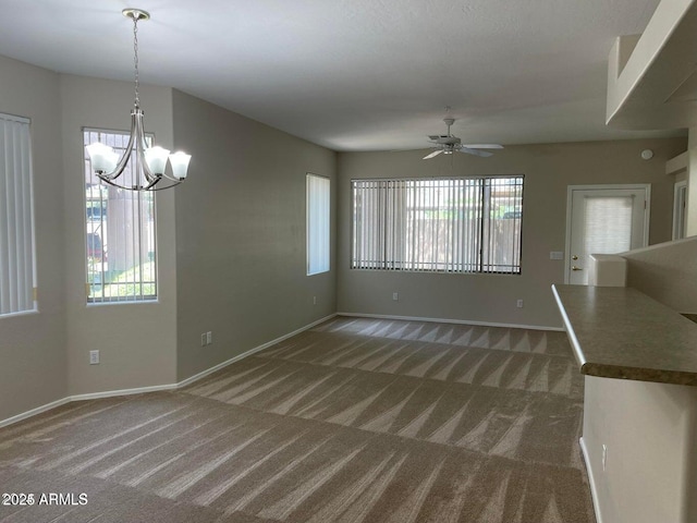 unfurnished living room featuring ceiling fan with notable chandelier, baseboards, and carpet floors