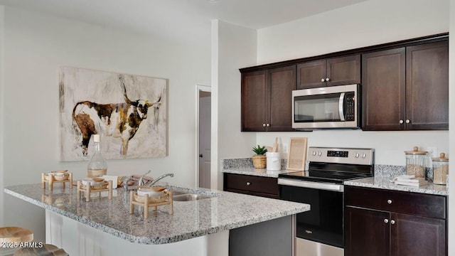 24052 W Pima St, Buckeye, AZ 85326 - kitchen featuring appliances with stainless steel finishes, dark brown cabinets, a kitchen bar, and light stone countertops