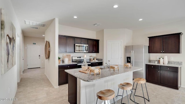 24052 W Pima St, Buckeye, AZ 85326 - kitchen featuring appliances with stainless steel finishes, a breakfast bar, dark brown cabinetry, light stone countertops, and recessed lighting