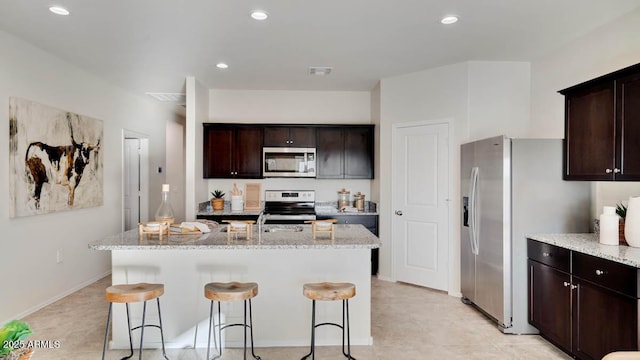 24052 W Pima St, Buckeye, AZ 85326 - kitchen featuring appliances with stainless steel finishes, light stone counters, a breakfast bar, an island with sink, and recessed lighting