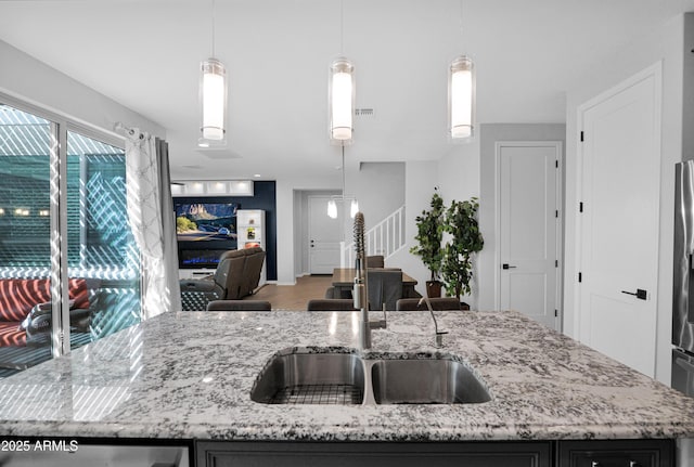 kitchen featuring a kitchen island with sink, light stone counters, open floor plan, and a sink