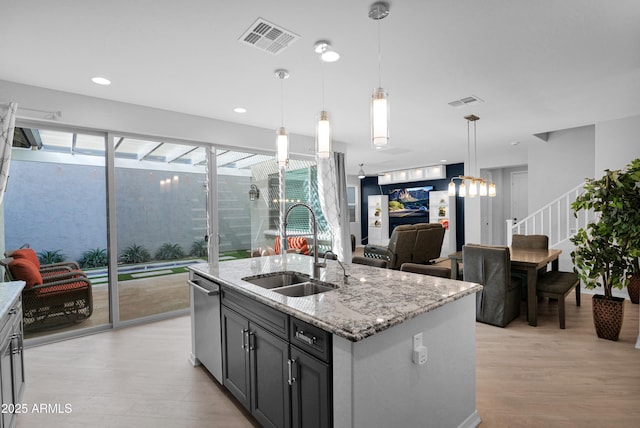 kitchen featuring visible vents, an island with sink, a sink, light stone counters, and light wood-style floors