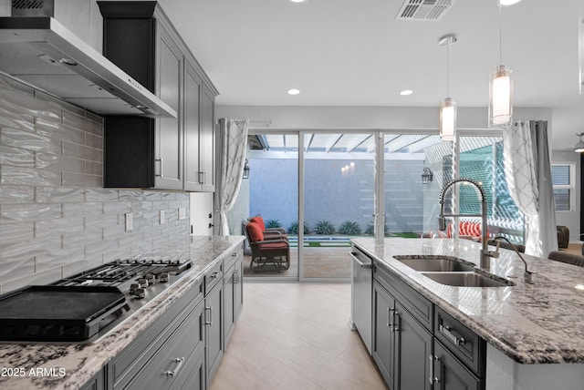 kitchen with light stone counters, visible vents, a sink, appliances with stainless steel finishes, and wall chimney exhaust hood