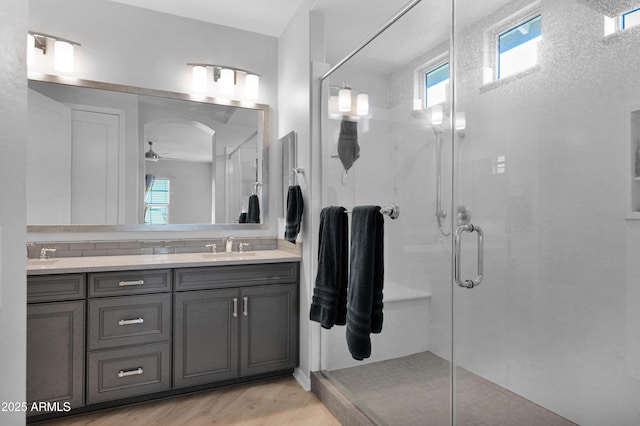 full bathroom with a sink, wood finished floors, a shower stall, double vanity, and ceiling fan