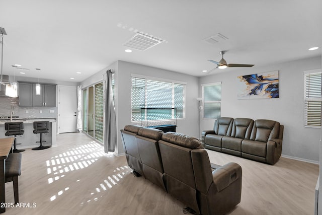 living room featuring visible vents, baseboards, a ceiling fan, and light wood finished floors