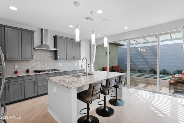 kitchen with wall chimney range hood, gray cabinetry, stainless steel gas cooktop, and a sink