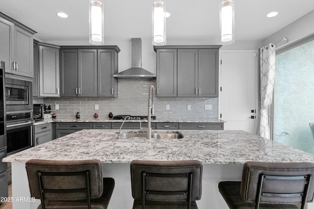 kitchen featuring stainless steel appliances, backsplash, gray cabinetry, and wall chimney range hood