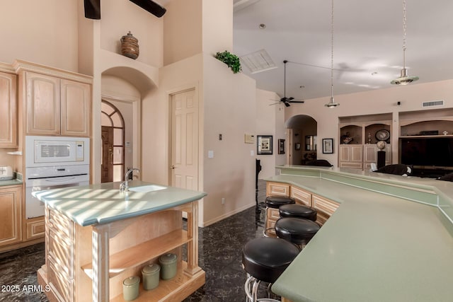 kitchen with white appliances, an island with sink, light brown cabinetry, and ceiling fan