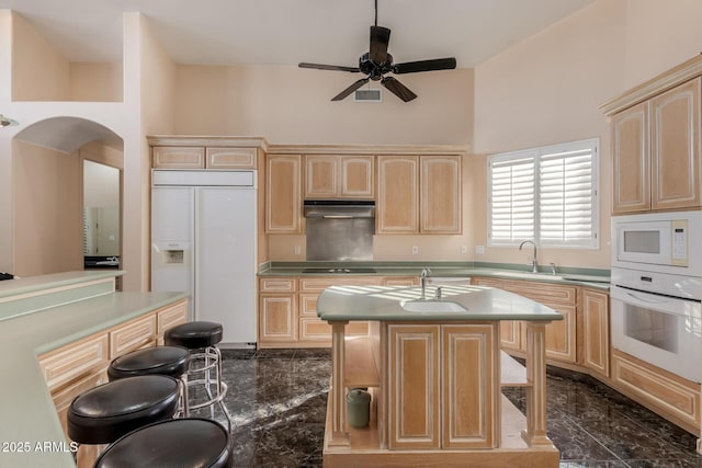 kitchen with built in appliances, ceiling fan, light brown cabinetry, a kitchen island, and a high ceiling