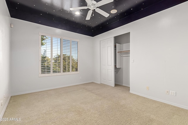 unfurnished bedroom with ceiling fan, light colored carpet, a closet, and a tray ceiling