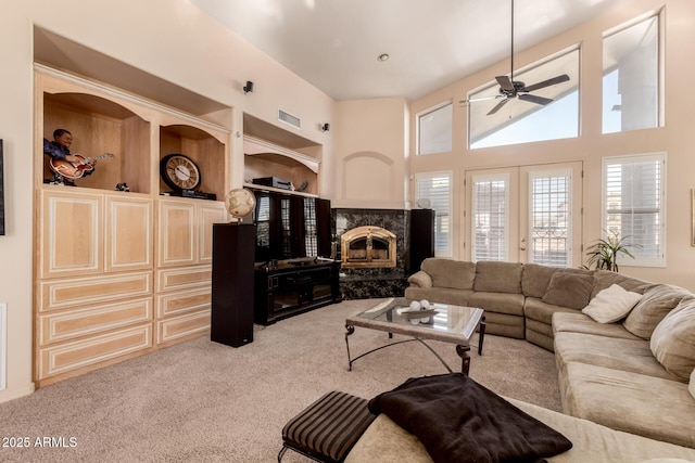 carpeted living room featuring a premium fireplace, a towering ceiling, ceiling fan, french doors, and built in features