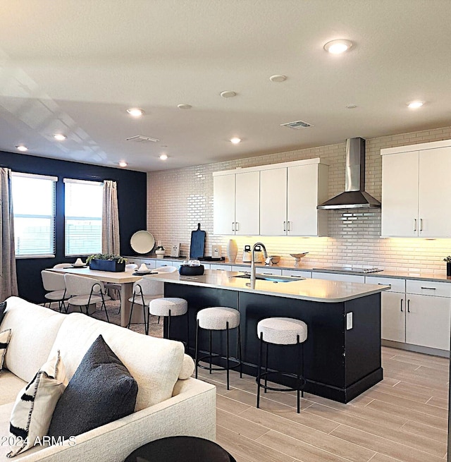 kitchen featuring white cabinets, a center island with sink, wall chimney exhaust hood, and sink