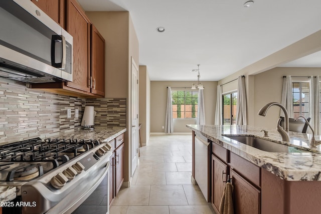 kitchen with stainless steel appliances, sink, light stone counters, backsplash, and pendant lighting