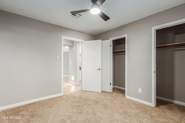 unfurnished bedroom featuring ceiling fan, light colored carpet, and two closets