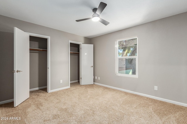 unfurnished bedroom featuring light carpet, ceiling fan, and multiple closets