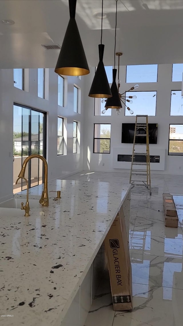 interior space featuring decorative light fixtures, light tile floors, light stone counters, and a high ceiling