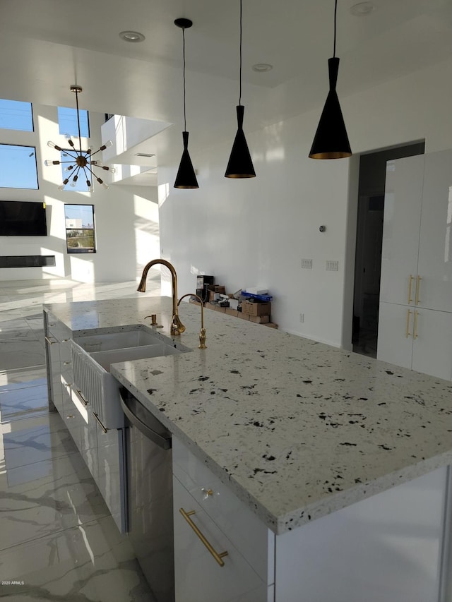 kitchen featuring light stone counters, white cabinets, stainless steel dishwasher, pendant lighting, and sink