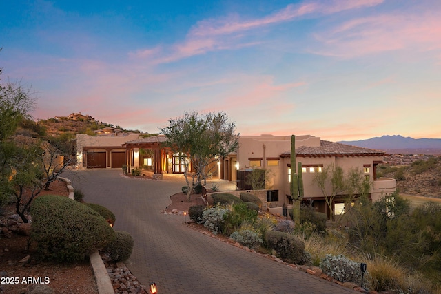 pueblo-style home featuring decorative driveway, an attached garage, and stucco siding