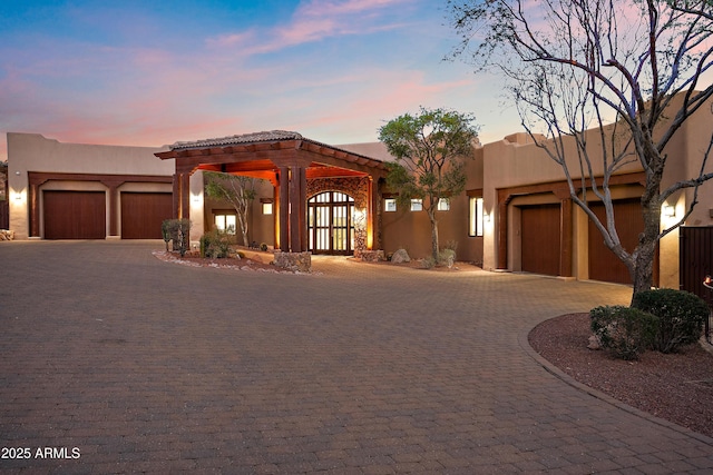 pueblo revival-style home featuring an attached garage, curved driveway, and stucco siding