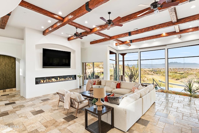 living room with beam ceiling, recessed lighting, stone tile flooring, a glass covered fireplace, and coffered ceiling