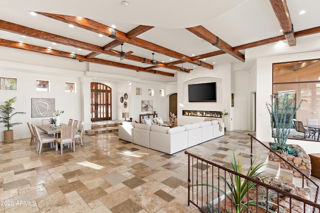 living room with stone tile floors, arched walkways, ceiling fan, beamed ceiling, and recessed lighting