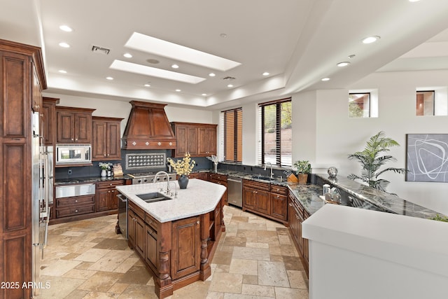 kitchen featuring a tray ceiling, appliances with stainless steel finishes, custom exhaust hood, and stone tile flooring