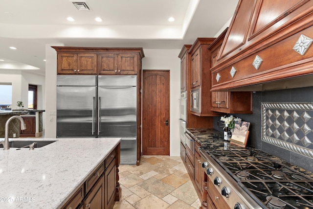 kitchen with a sink, visible vents, stovetop, stainless steel built in refrigerator, and stone tile flooring