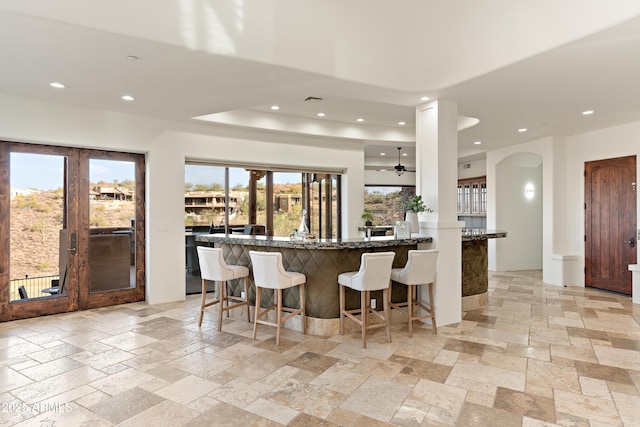 kitchen featuring dark stone counters, a kitchen breakfast bar, stone tile flooring, and recessed lighting