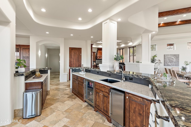 kitchen featuring arched walkways, stone tile floors, recessed lighting, a sink, and beverage cooler