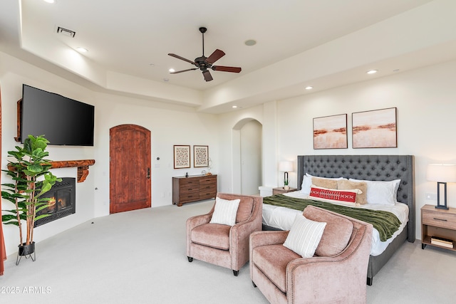 bedroom with light carpet, visible vents, arched walkways, a glass covered fireplace, and recessed lighting