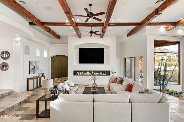 living room with ornate columns, stone tile floors, beam ceiling, and a glass covered fireplace