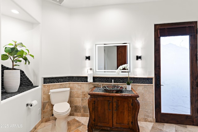 bathroom with a wainscoted wall, tile walls, toilet, and vanity