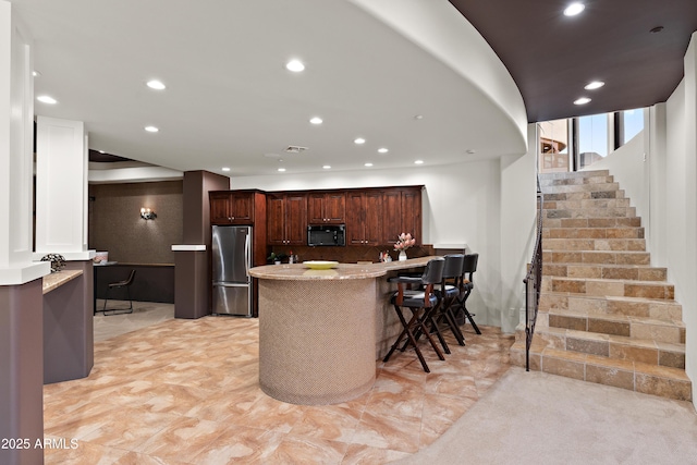 kitchen featuring black microwave, recessed lighting, a peninsula, a breakfast bar, and freestanding refrigerator