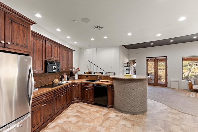 kitchen featuring recessed lighting, a peninsula, a sink, black appliances, and tasteful backsplash