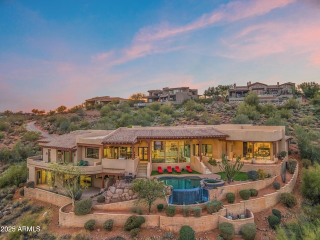 rear view of property with a tile roof, stucco siding, a pool with connected hot tub, a patio area, and stairs