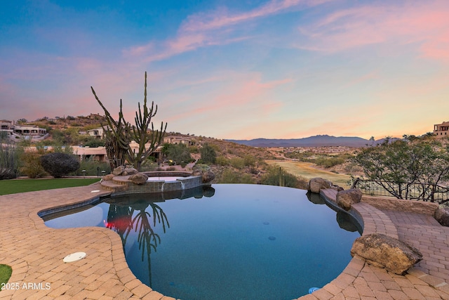 view of swimming pool featuring a pool with connected hot tub, a patio area, fence, and a mountain view