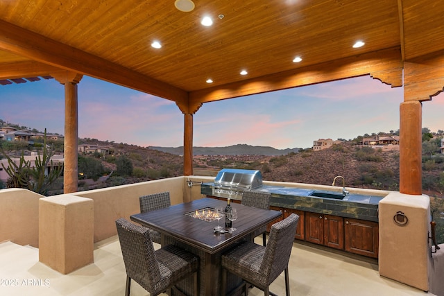 patio terrace at dusk featuring exterior kitchen, outdoor dining space, a grill, and a sink