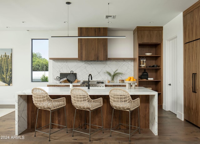 kitchen with dark hardwood / wood-style flooring, an island with sink, range, pendant lighting, and tasteful backsplash